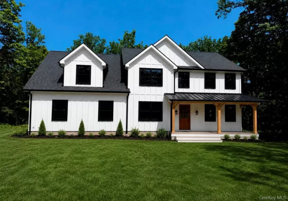 Modern farmhouse exterior featuring board and batten siding, a covered porch with wooden beams, black-framed windows, and a black metal roof accent Modern farmhouse exterior featuring board and batten siding, a covered porch with wooden beams, black-framed windows, and a black metal roof accent