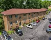Brick facade building featuring multiple residential units, a red shingle roof, and a dedicated asphalt parking area with marked spaces Brick facade building featuring multiple residential units, a red shingle roof, and a dedicated asphalt parking area with marked spaces