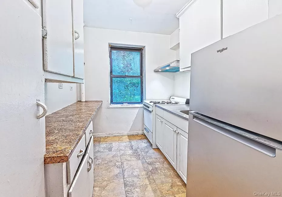 Galley kitchen featuring white cabinetry, patterned countertops, and a window Galley kitchen featuring white cabinetry, patterned countertops, and a window