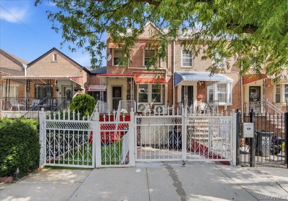 Brick facade residence featuring a white decorative metal fence and gate, an awning over the front entrance, and an additional white awning over the bay window Brick facade residence featuring a white decorative metal fence and gate, an awning over the front entrance, and an additional white awning over the bay window
