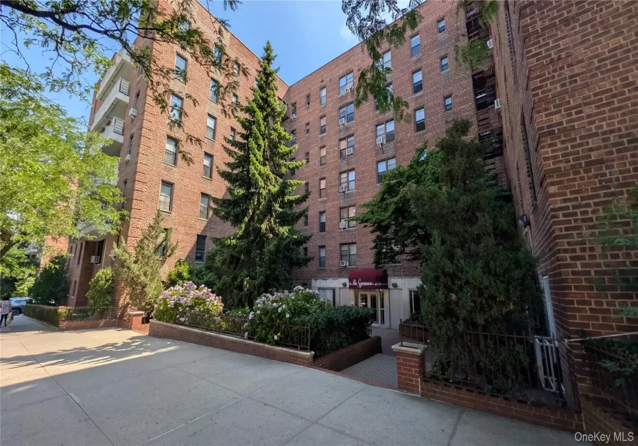 Brick multi-story building featuring multiple balconies, mature landscaping, and a covered entrance with an awning Brick multi-story building featuring multiple balconies, mature landscaping, and a covered entrance with an awning