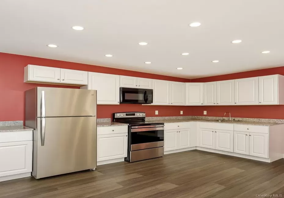 Kitchen featuring stainless steel appliances, recessed lighting, white cabinetry, dark wood-style flooring, and light stone counters Kitchen featuring stainless steel appliances, recessed lighting, white cabinetry, dark wood-style flooring, and light stone counters