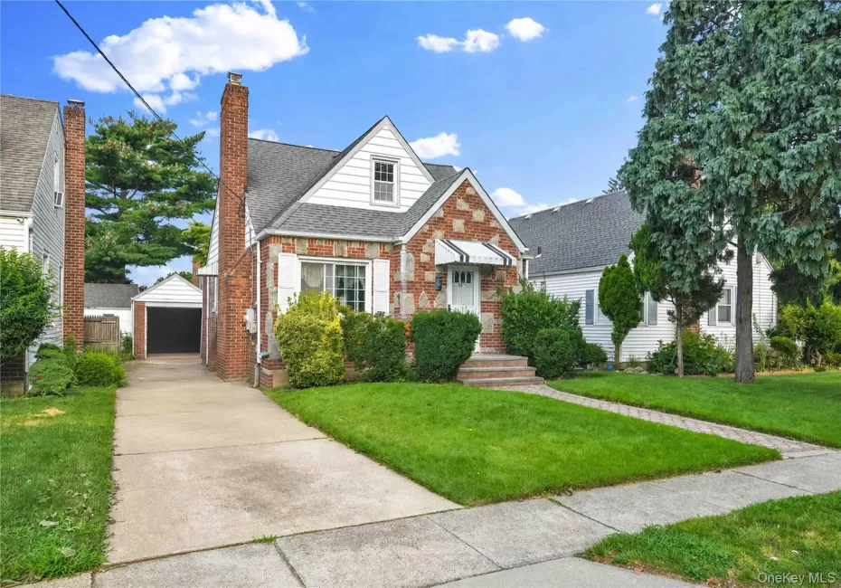 Charming brick Colonial with crisp white trim and peaked roofline, featuring a manicured front lawn, established landscaping with mature shrubs, concrete driveway, and a single-car garage Charming brick Colonial with crisp white trim and peaked roofline, featuring a manicured front lawn, established landscaping with mature shrubs, concrete driveway, and a single-car garage