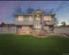 Elevated colonial-style home featuring a manicured lawn, vinyl siding exterior, brick foundation detailing, white vinyl fencing, and illuminated front entrance with peaked gable roof and covered front porch Elevated colonial-style home featuring a manicured lawn, vinyl siding exterior, brick foundation detailing, white vinyl fencing, and illuminated front entrance with peaked gable roof and covered front porch