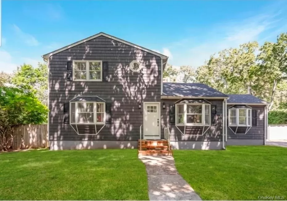 Shingle-sided exterior with a white entry door, three bay windows, black window shutters, and a well-maintained front lawn Shingle-sided exterior with a white entry door, three bay windows, black window shutters, and a well-maintained front lawn