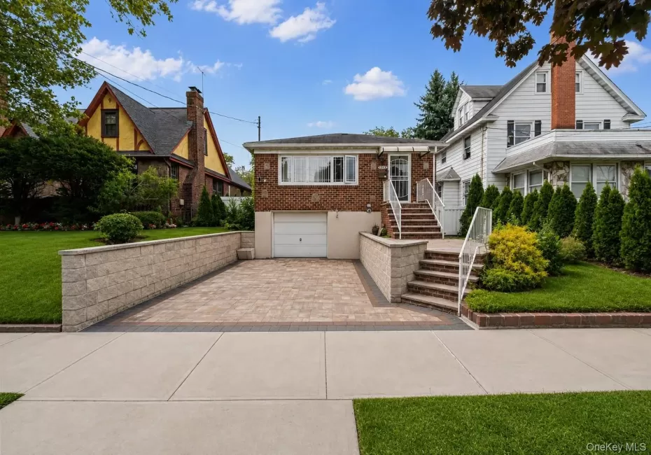 Brick exterior with a white garage door, paved driveway, and stone retaining walls Brick exterior with a white garage door, paved driveway, and stone retaining walls
