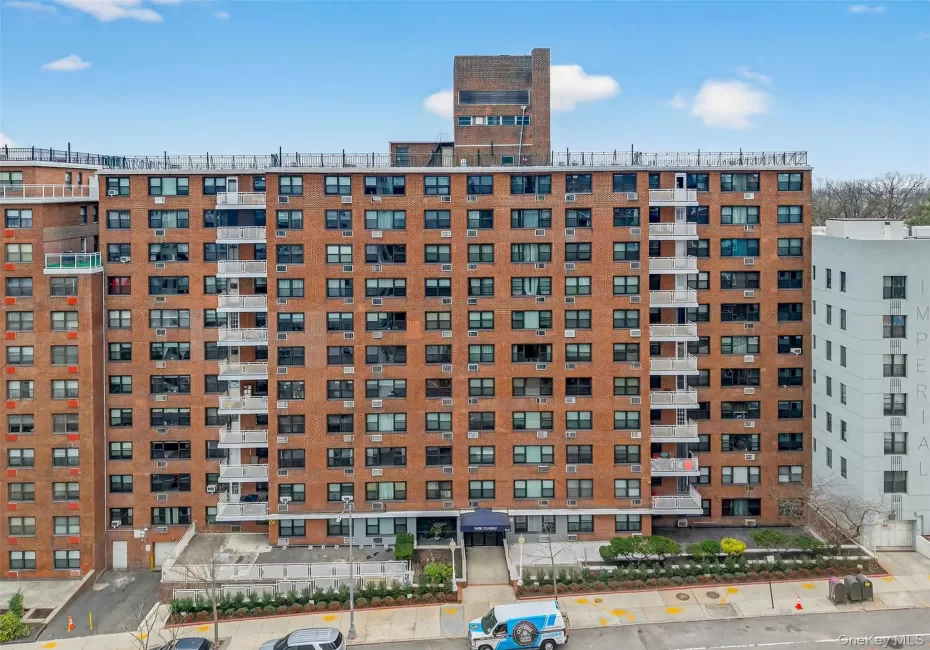 Brick facade building with multiple balconies, a ground-level entrance canopy, and structured landscaping Brick facade building with multiple balconies, a ground-level entrance canopy, and structured landscaping