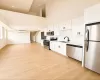 Open-concept living space featuring wood-finish flooring, a kitchen with stainless steel appliances and white cabinetry, and high vaulted ceilings Open-concept living space featuring wood-finish flooring, a kitchen with stainless steel appliances and white cabinetry, and high vaulted ceilings