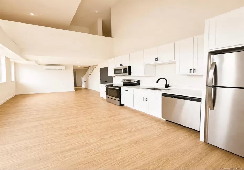 Open-concept living space featuring wood-finish flooring, a kitchen with stainless steel appliances and white cabinetry, and high vaulted ceilings Open-concept living space featuring wood-finish flooring, a kitchen with stainless steel appliances and white cabinetry, and high vaulted ceilings