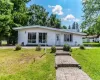 White siding exterior with a sloped roofline, large picture windows, and a brick paver walkway leading to the entrance White siding exterior with a sloped roofline, large picture windows, and a brick paver walkway leading to the entrance
