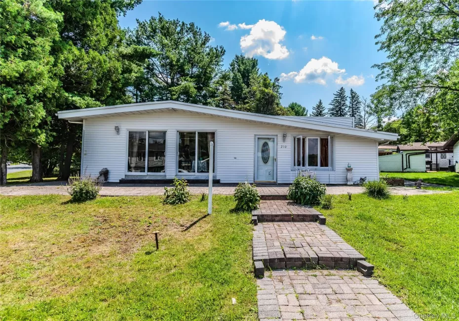 White siding exterior with a sloped roofline, large picture windows, and a brick paver walkway leading to the entrance White siding exterior with a sloped roofline, large picture windows, and a brick paver walkway leading to the entrance