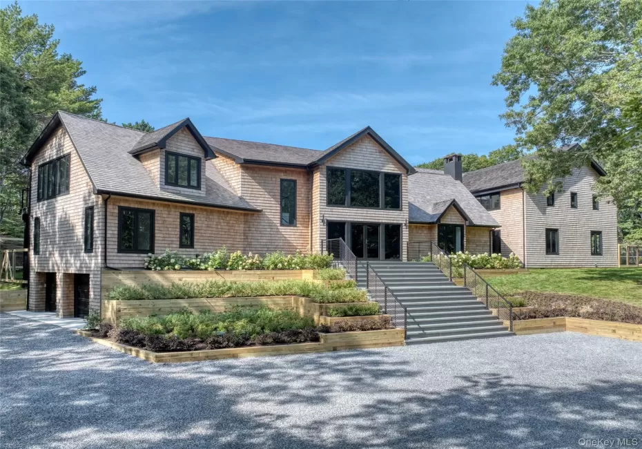 Shingle-style exterior with black trim windows, multi-level tiered landscaping, broad front steps, and a gravel driveway Shingle-style exterior with black trim windows, multi-level tiered landscaping, broad front steps, and a gravel driveway