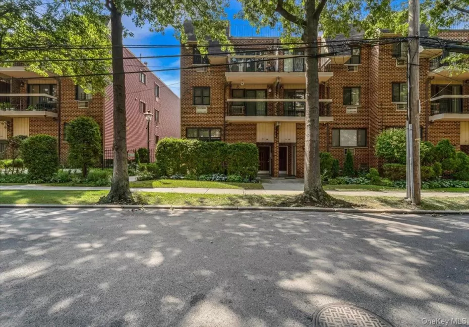 Brick facade building with multiple balconies, manicured landscaping, and mature trees Brick facade building with multiple balconies, manicured landscaping, and mature trees