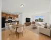 Open-concept living space featuring wood-finish flooring, a kitchen with wood cabinetry and black appliances, a dining area, and a living area with large windows Open-concept living space featuring wood-finish flooring, a kitchen with wood cabinetry and black appliances, a dining area, and a living area with large windows