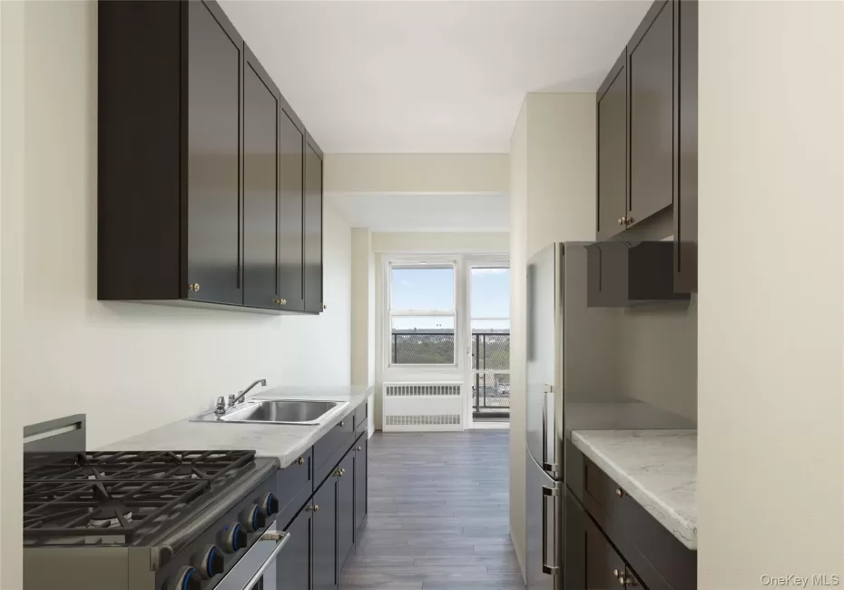 Galley kitchen featuring dark cabinetry with brushed metal hardware, gas cooktop with multiple burners, stainless steel sink, and quartz countertops Galley kitchen featuring dark cabinetry with brushed metal hardware, gas cooktop with multiple burners, stainless steel sink, and quartz countertops