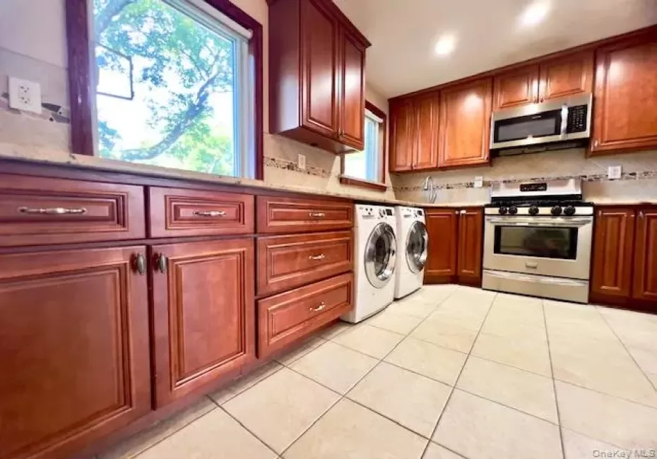 Kitchen with stainless steel appliances, washer and clothes dryer, light tile patterned floors, decorative backsplash, and light stone countertops Kitchen with stainless steel appliances, washer and clothes dryer, light tile patterned floors, decorative backsplash, and light stone countertops
