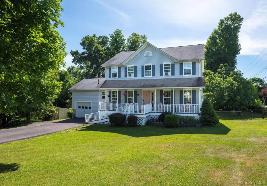 Two-story residence featuring light blue siding, a covered front porch with white railing, and an attached single-car garage Two-story residence featuring light blue siding, a covered front porch with white railing, and an attached single-car garage