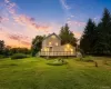 Expansive green lawn surrounds a two-story residence with a wraparound wood deck and exterior lighting Expansive green lawn surrounds a two-story residence with a wraparound wood deck and exterior lighting