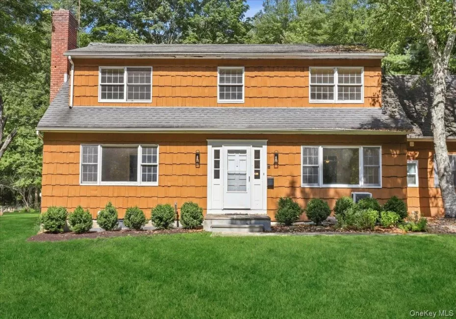 Wood shingle siding exterior with multiple windows, a prominent brick chimney, and a white paneled front door Wood shingle siding exterior with multiple windows, a prominent brick chimney, and a white paneled front door