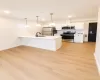 Kitchen featuring stainless steel appliances, white cabinetry, a kitchen island with sink, three pendant lights, and wood-finish flooring Kitchen featuring stainless steel appliances, white cabinetry, a kitchen island with sink, three pendant lights, and wood-finish flooring