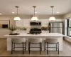 Kitchen featuring a central island with an integrated sink, three pendant lights, white cabinetry, stainless steel appliances, and wood-finish flooring Kitchen featuring a central island with an integrated sink, three pendant lights, white cabinetry, stainless steel appliances, and wood-finish flooring