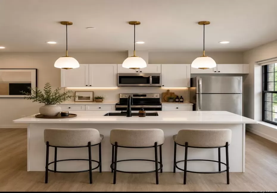 Kitchen featuring a central island with an integrated sink, three pendant lights, white cabinetry, stainless steel appliances, and wood-finish flooring Kitchen featuring a central island with an integrated sink, three pendant lights, white cabinetry, stainless steel appliances, and wood-finish flooring
