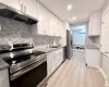 White shaker cabinetry, light wood-finish flooring, stainless steel appliances, stone countertops, and a full tile backsplash White shaker cabinetry, light wood-finish flooring, stainless steel appliances, stone countertops, and a full tile backsplash