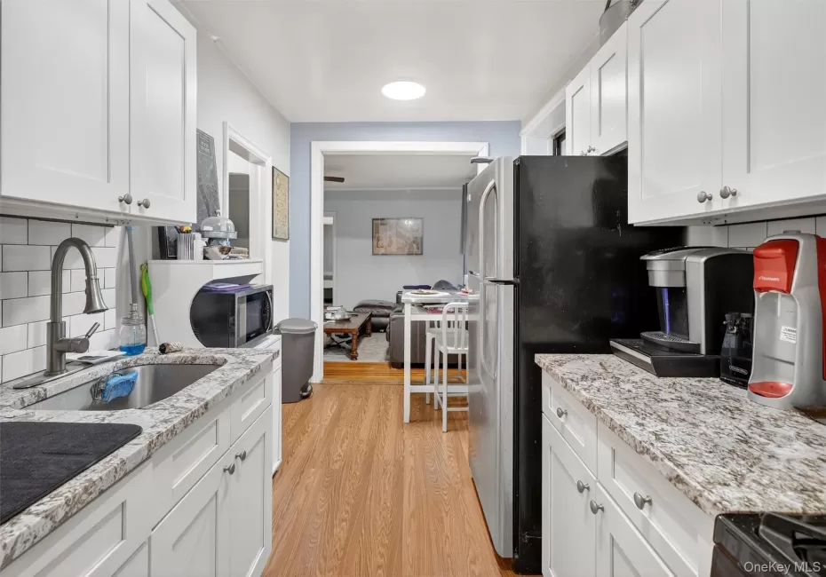 Kitchen with decorative backsplash, white cabinets, light stone counters, and black appliances Kitchen with decorative backsplash, white cabinets, light stone counters, and black appliances