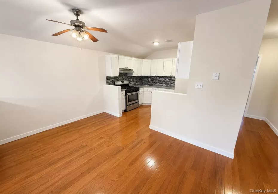 Wood-finish flooring, ceiling fan with integrated lighting, white cabinetry, stainless steel range, and tile backsplash Wood-finish flooring, ceiling fan with integrated lighting, white cabinetry, stainless steel range, and tile backsplash