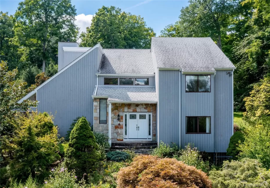 Contemporary exterior featuring vertical siding, a stone facade entry, a gabled roofline, and ample natural landscaping Contemporary exterior featuring vertical siding, a stone facade entry, a gabled roofline, and ample natural landscaping