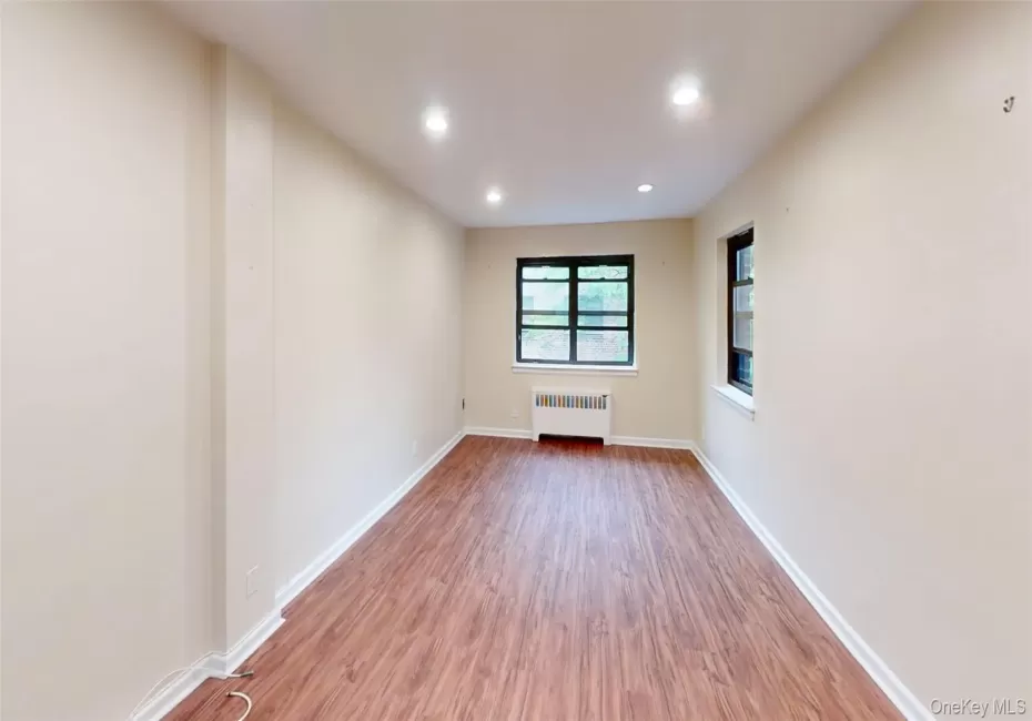 Unfurnished room with radiator heating unit, wood finished floors, recessed lighting, and baseboards Unfurnished room with radiator heating unit, wood finished floors, recessed lighting, and baseboards