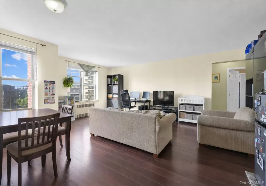 Expansive living area with wood-finish flooring, multiple windows, and a built-in wall-mounted radiator Expansive living area with wood-finish flooring, multiple windows, and a built-in wall-mounted radiator