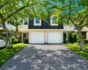 Exterior featuring a dark shingle roof, light-colored siding, stone accents, two white garage doors, and a paved driveway Exterior featuring a dark shingle roof, light-colored siding, stone accents, two white garage doors, and a paved driveway