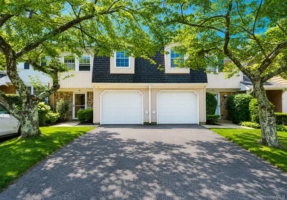 Exterior featuring a dark shingle roof, light-colored siding, stone accents, two white garage doors, and a paved driveway Exterior featuring a dark shingle roof, light-colored siding, stone accents, two white garage doors, and a paved driveway