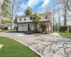 Two-story residence with a two-car garage, circular driveway with paver accents, front porch, and mature trees Two-story residence with a two-car garage, circular driveway with paver accents, front porch, and mature trees