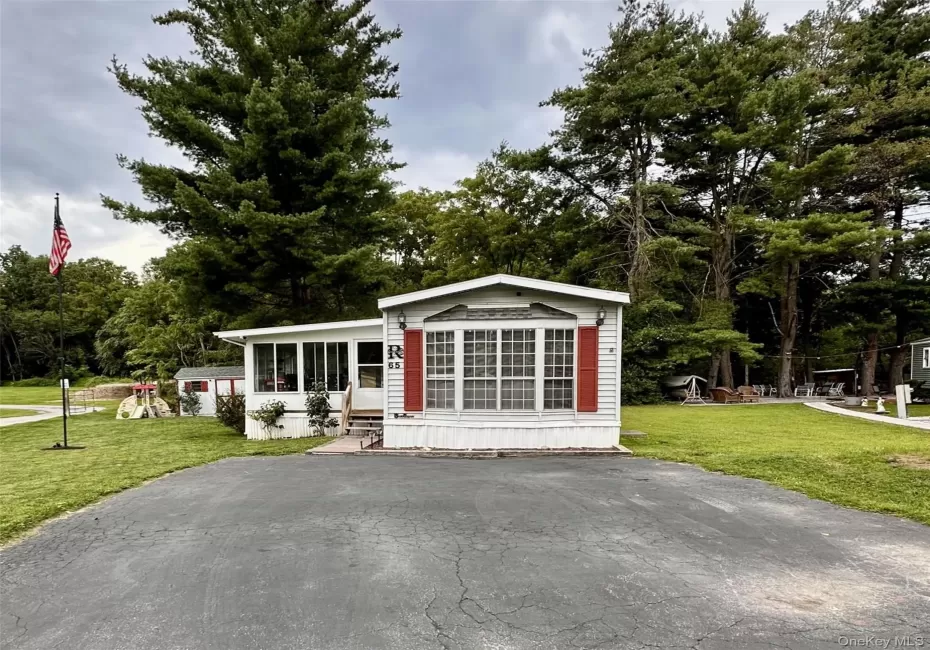 White siding exterior featuring a sunroom, bay window with red shutters, and an asphalt driveway. White siding exterior featuring a sunroom, bay window with red shutters, and an asphalt driveway.