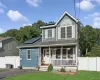 Two-story exterior with blue siding, a covered front porch, an arched window, and solar panels Two-story exterior with blue siding, a covered front porch, an arched window, and solar panels