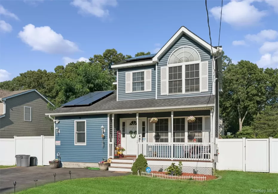 Two-story exterior with blue siding, a covered front porch, an arched window, and solar panels Two-story exterior with blue siding, a covered front porch, an arched window, and solar panels