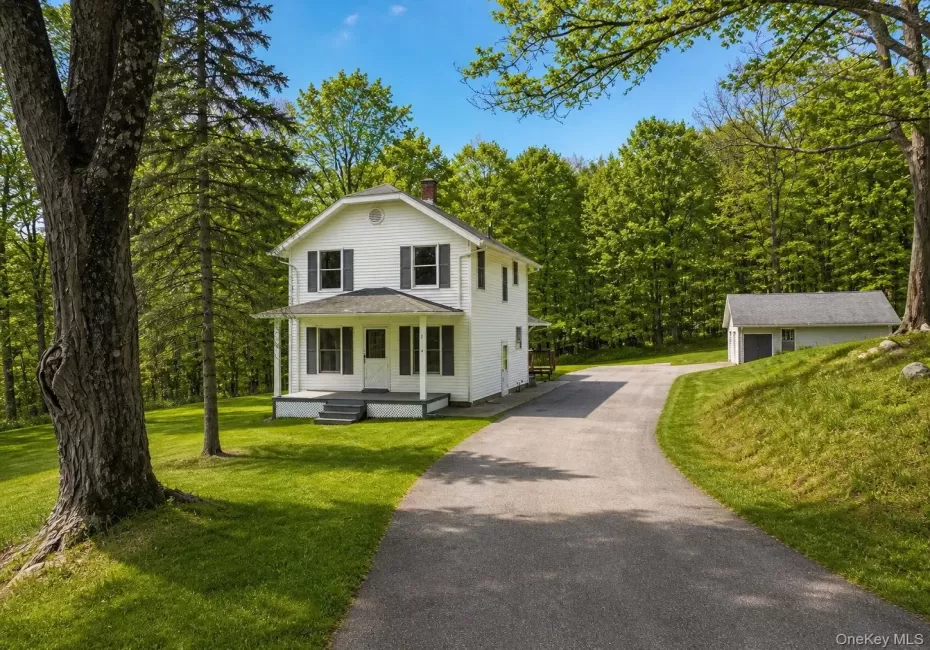 Two-story white residence featuring a covered front porch, black window shutters, and a grey asphalt driveway Two-story white residence featuring a covered front porch, black window shutters, and a grey asphalt driveway