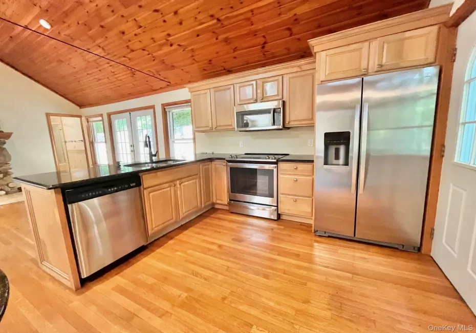 Kitchen with stainless steel appliances, a sink, wooden ceiling, light wood finished floors, and dark countertops Kitchen with stainless steel appliances, a sink, wooden ceiling, light wood finished floors, and dark countertops