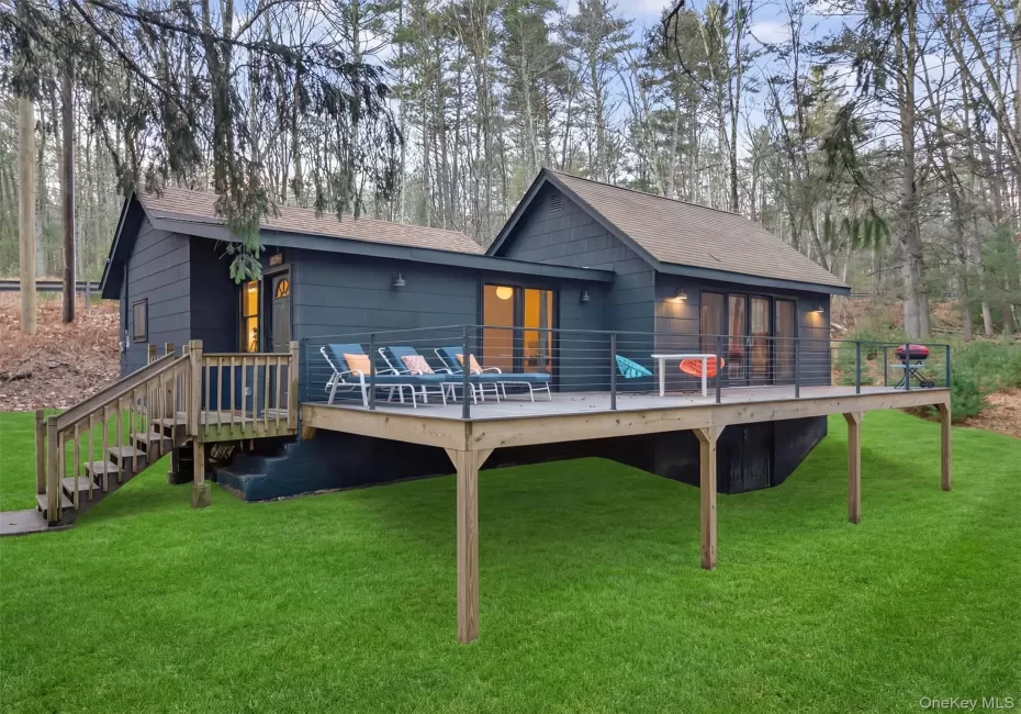Back of property with a lawn, a wooden deck, and roof with shingles Back of property with a lawn, a wooden deck, and roof with shingles