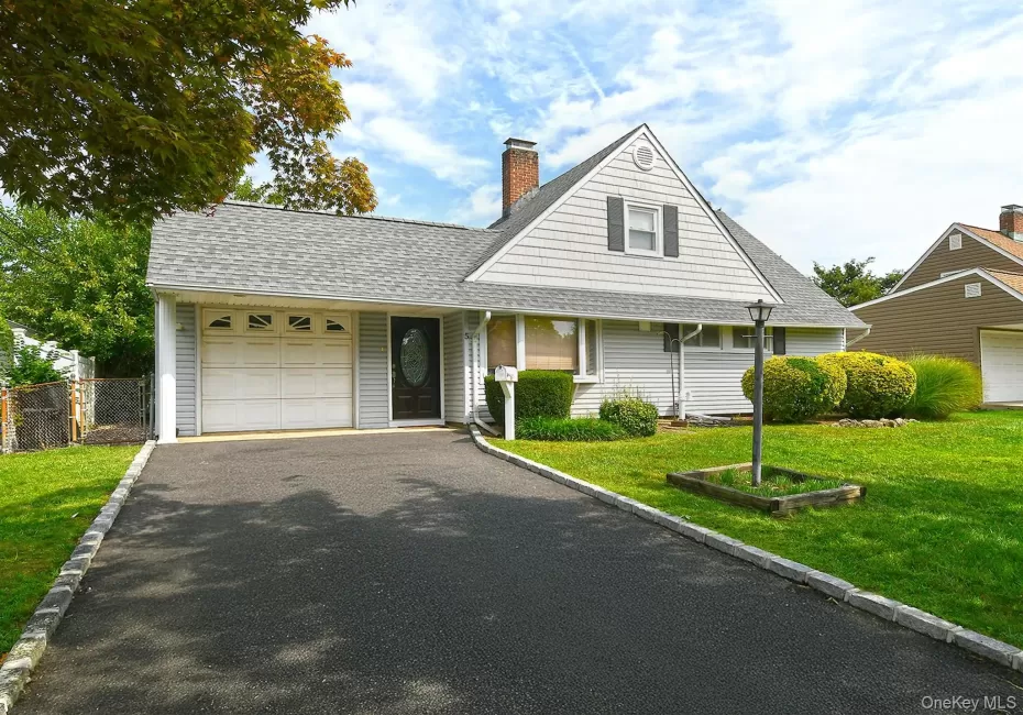 Light-colored siding exterior with a dark entry door, attached garage with panel door, asphalt driveway, and a well-maintained lawn Light-colored siding exterior with a dark entry door, attached garage with panel door, asphalt driveway, and a well-maintained lawn