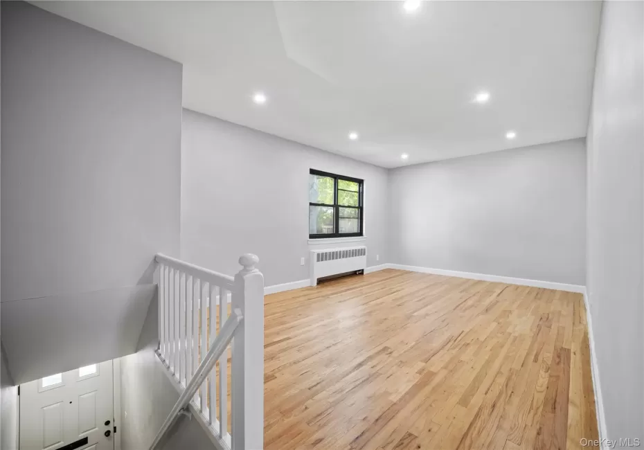Recessed lighting, wood-finish flooring, staircase with white balustrade, window with black trim, and a radiator Recessed lighting, wood-finish flooring, staircase with white balustrade, window with black trim, and a radiator