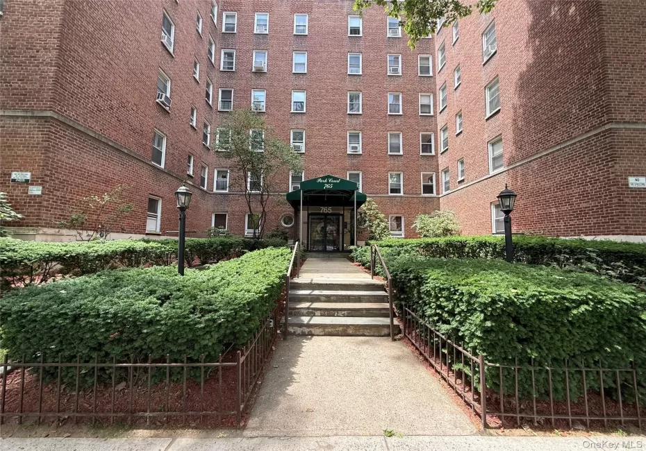 Brick exterior multi-story building featuring a central entrance with a green awning and integrated lighting Brick exterior multi-story building featuring a central entrance with a green awning and integrated lighting