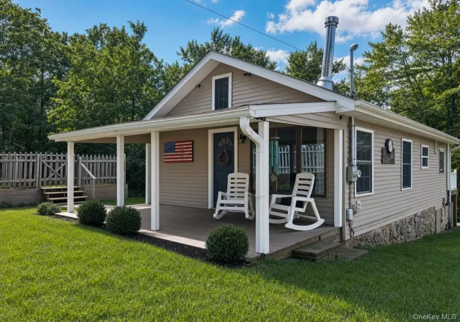 Covered front porch with decking, tan siding, multiple windows, and a stone foundation Covered front porch with decking, tan siding, multiple windows, and a stone foundation