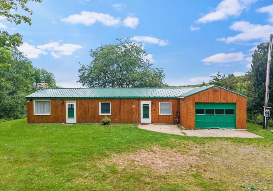 Wood-paneled exterior with a green metal roof, integrated garage featuring a green door, and multiple entry points Wood-paneled exterior with a green metal roof, integrated garage featuring a green door, and multiple entry points