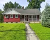 Red-sided residence featuring a covered front porch with white railings, a front-facing gable with vertical siding, and a stone-paved walkway Red-sided residence featuring a covered front porch with white railings, a front-facing gable with vertical siding, and a stone-paved walkway