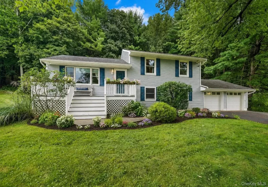 Split-level residence featuring gray siding, a two-car garage, and a front deck with lattice detailing Split-level residence featuring gray siding, a two-car garage, and a front deck with lattice detailing