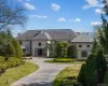 Grand estate featuring a circular driveway, manicured landscaping, a slate-style roof, a portico entrance, and an upper-level balcony with balustrade Grand estate featuring a circular driveway, manicured landscaping, a slate-style roof, a portico entrance, and an upper-level balcony with balustrade