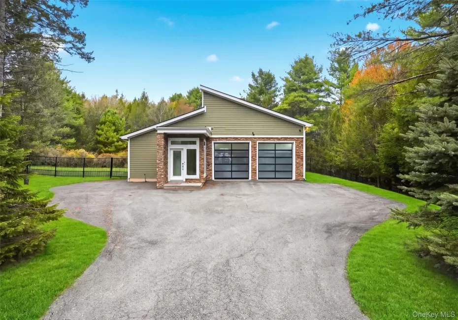 Modern ranch-style home featuring a four-car garage with frosted glass doors, a stone facade accent, and a light green exterior Modern ranch-style home featuring a four-car garage with frosted glass doors, a stone facade accent, and a light green exterior